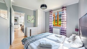 Een slaapkamer met een bed, nachtkastje, raam met gordijnen en uitzicht op de omgeving.