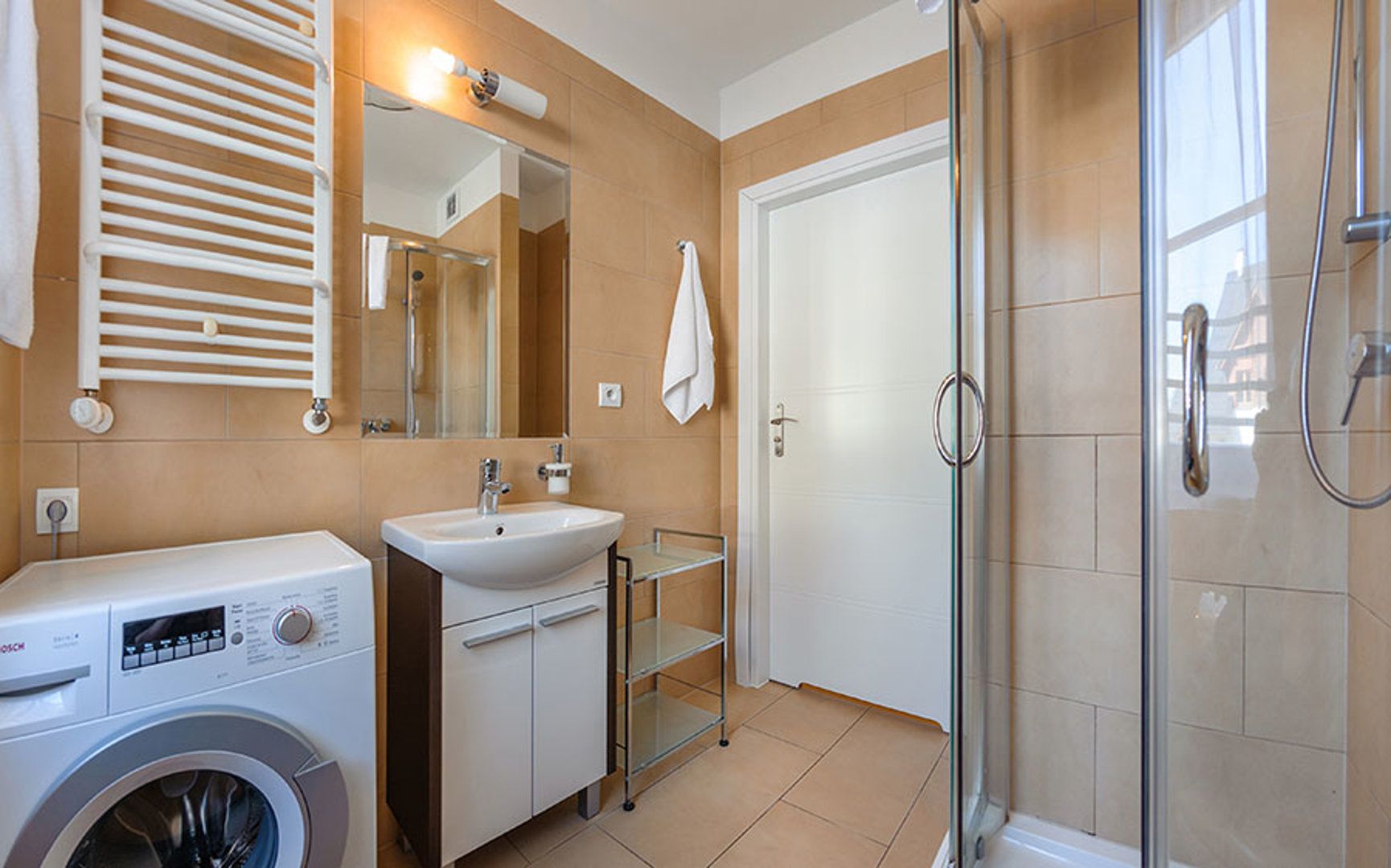 Une salle de bain moderne équipée d’un lave-linge, d’un lavabo et d’une douche à parois en verre.