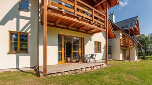 Een houten huis met twee verdiepingen, een balkon, grote ramen en een patio.