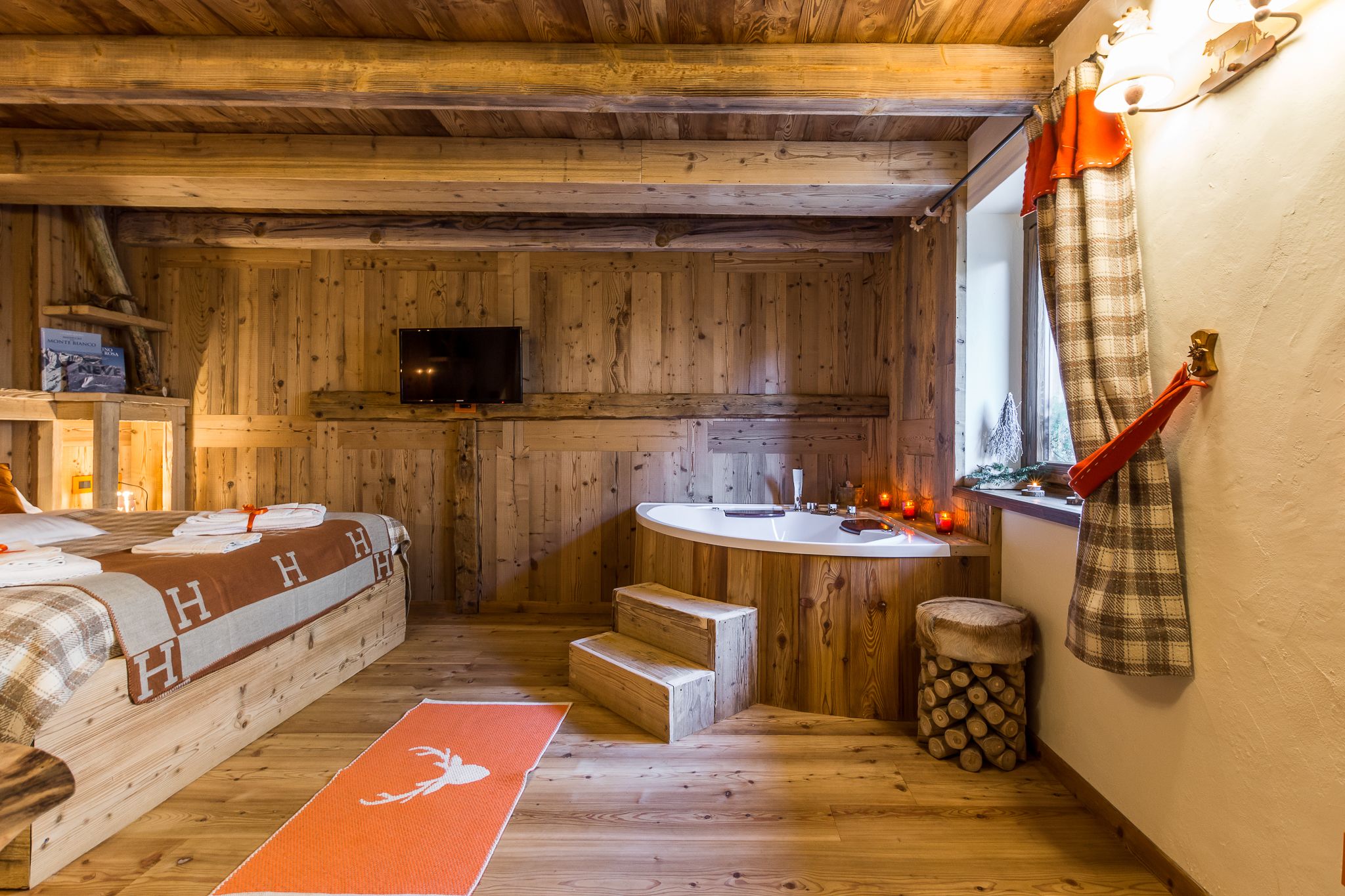 Una habitación de cabaña acogedora con interior de madera, una cama, un baño pequeño con lavamanos y una ventana con cortinas.