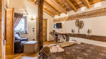 Una habitación acogedora con techo de madera, una cama con colcha estampada, una silla, una mesita con televisor y una ventana con cortinas.