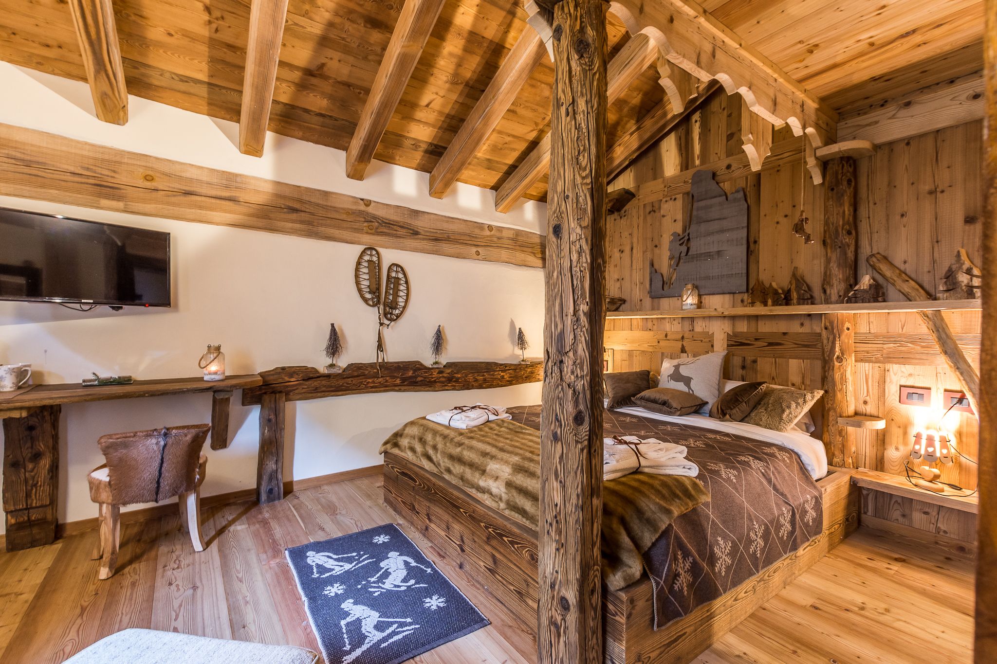 A rustic wooden room with a bed, a desk, and a television.