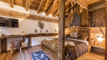 A rustic wooden room with a bed, a desk, and a television.