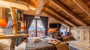 A cozy room with a wooden ceiling, a bed with plaid bedding, a wooden table with a lamp, and a window with curtains. - Affittacamere Annie-Parblanc (La Salle)