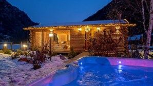A wooden cabin with a hot tub and a deck, surrounded by snow and mountains. - Affittacamere Annie-Parblanc (La Salle)