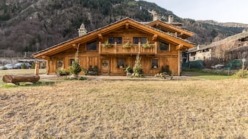 Una cabaña de madera con balcón, rodeada por un campo seco y montañas.