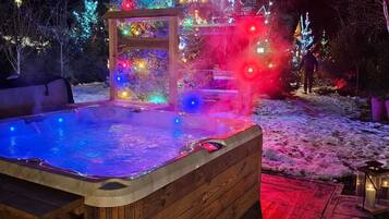 A hot tub with a wooden frame, surrounded by a snow-covered deck.