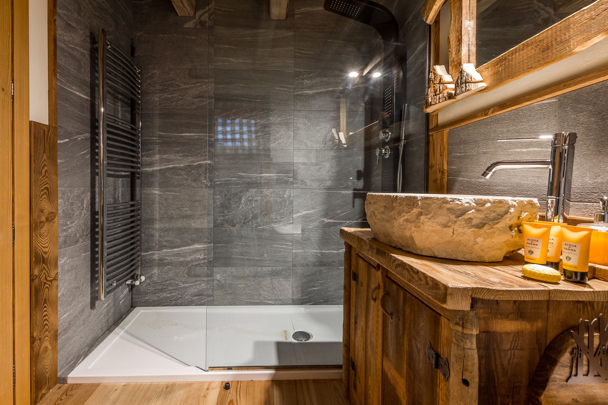 A modern bathroom with a glass-enclosed shower, a wooden vanity, and a large stone basin.