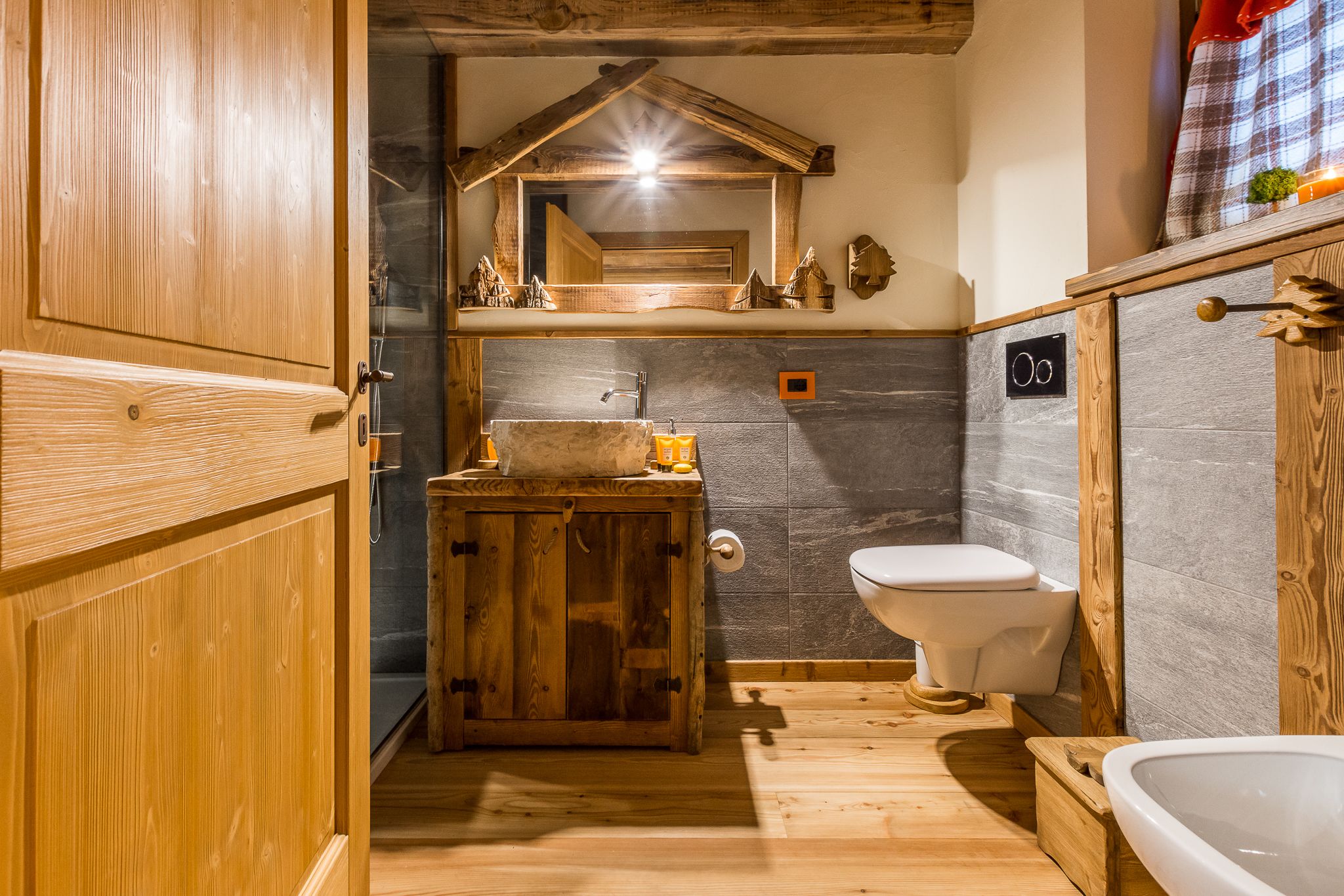 A rustic bathroom with wooden cabinetry, a stone sink, and a white toilet.