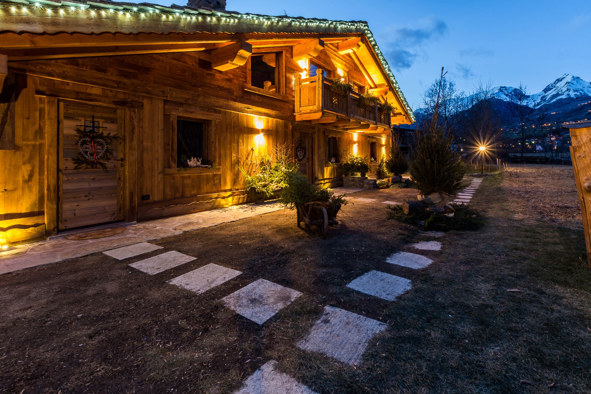 A wooden chalet with a balcony, a wooden door with a wreath, and a path leading to the entrance.
