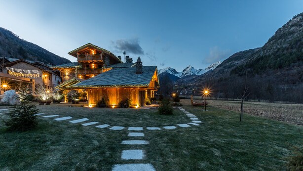 A rustic chalet with a stone pathway leading to the entrance, surrounded by mountains and lit by warm lights. - Affittacamere Annie-Parblanc (La Salle)