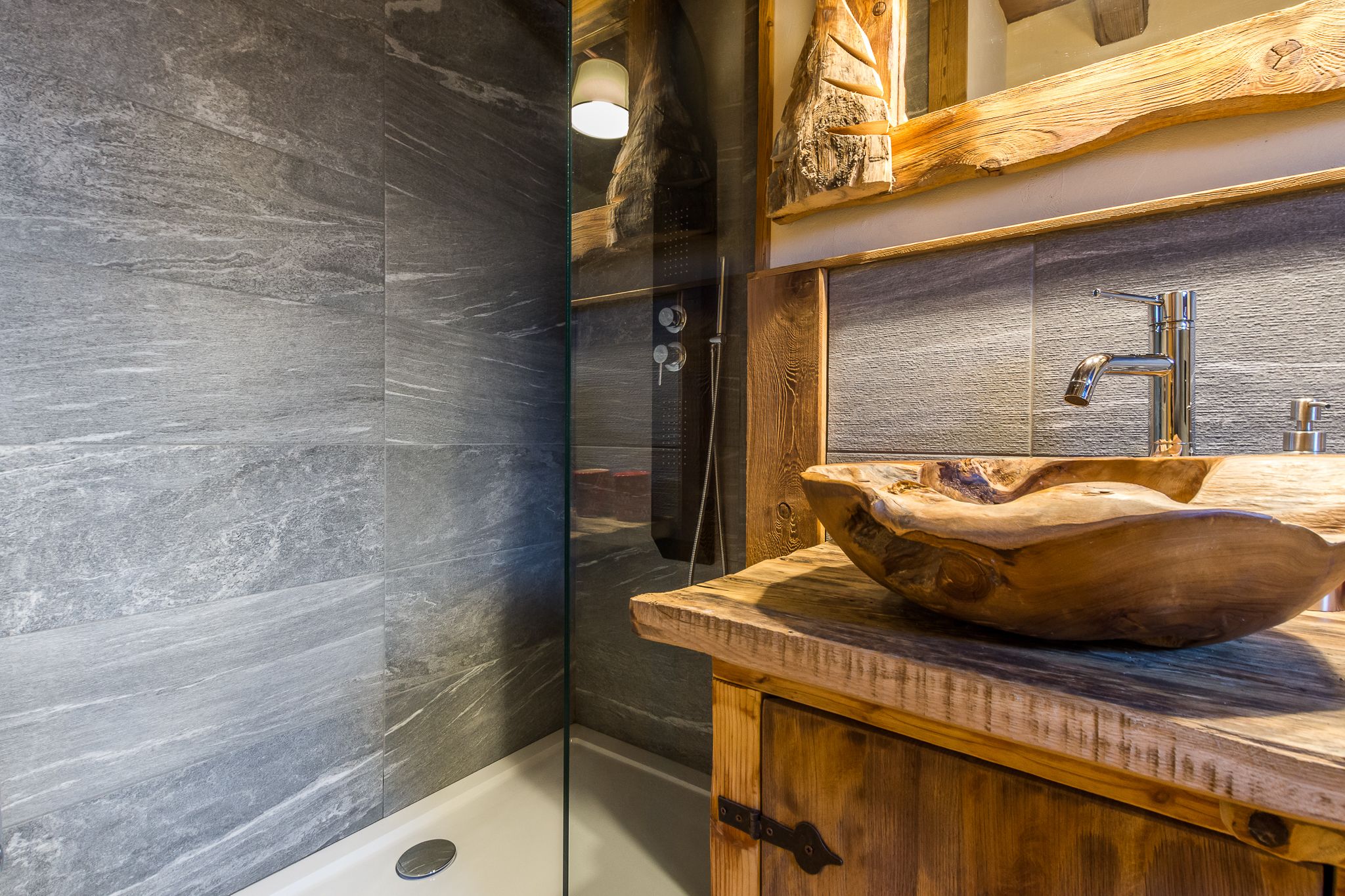 A bathroom with a large, rustic wooden bowl sink, a glass shower enclosure, and a wooden vanity with a mirror above the sink.