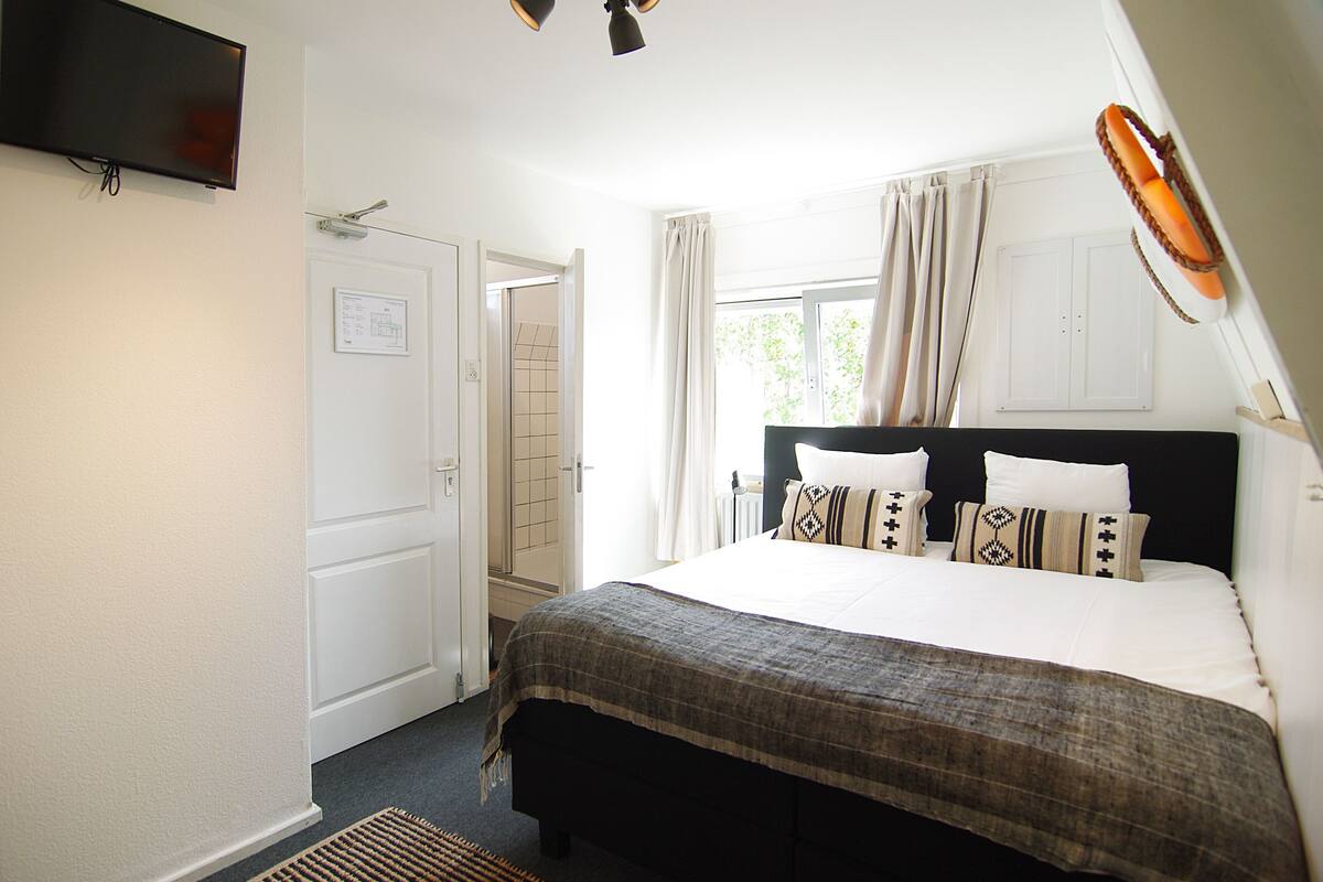 A bedroom with a bed, a television mounted on the wall, and a window with curtains.