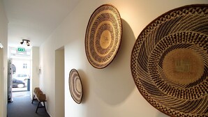 A hallway with three large woven baskets on the wall, a bench, and a door leading outside. - Hotel Zand (Zandvoort)