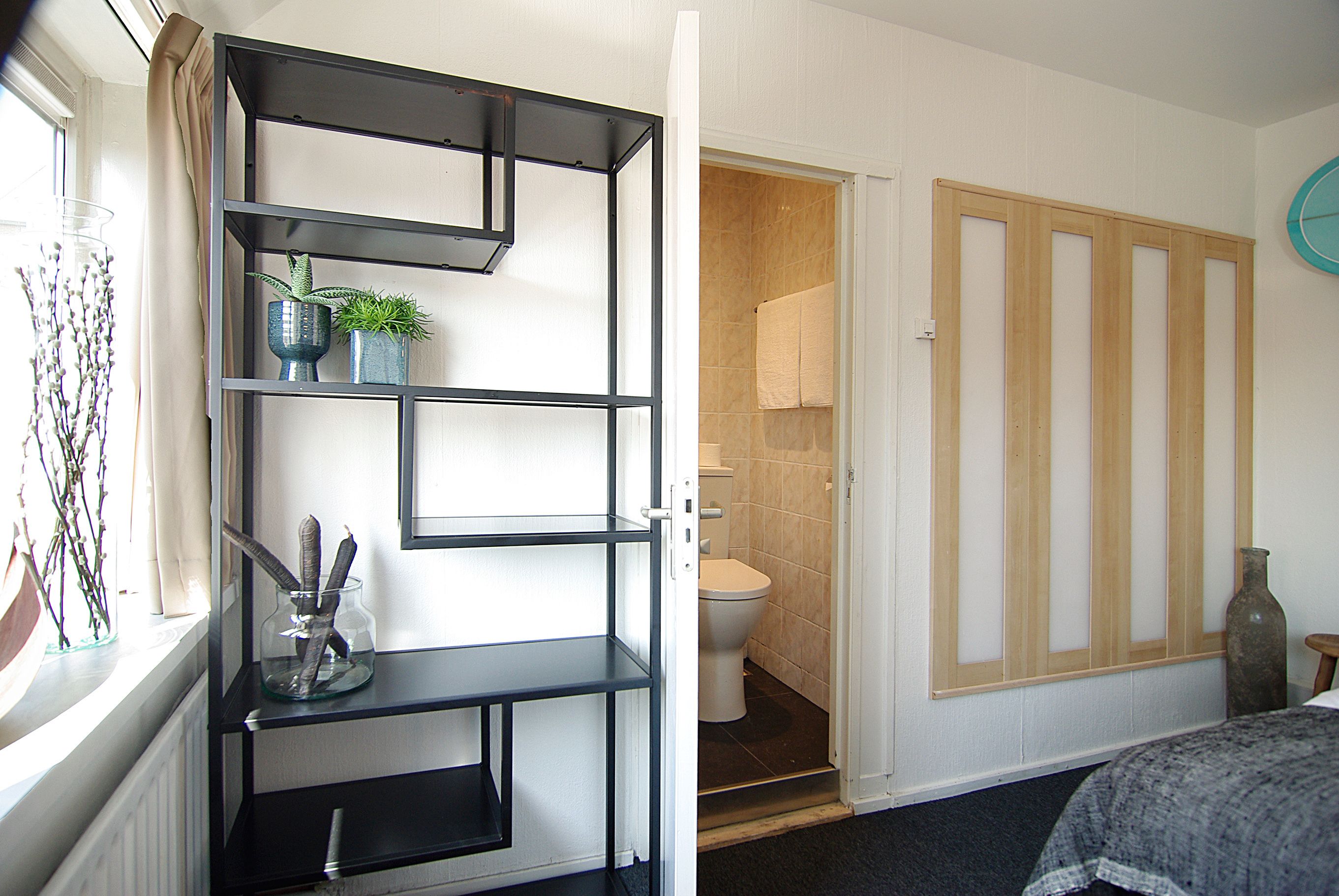 Una habitación con una estantería metálica negra, un inodoro y una puerta de madera.