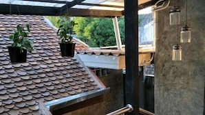 Ett takförsett utomhusområde med ett metallräcke, planterade växter och hängande lampor.