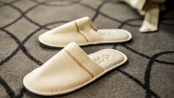 Un par de zapatillas color beige con un estampado texturizado y un pequeño diseño bordado en la suela, sobre un suelo con motivos.