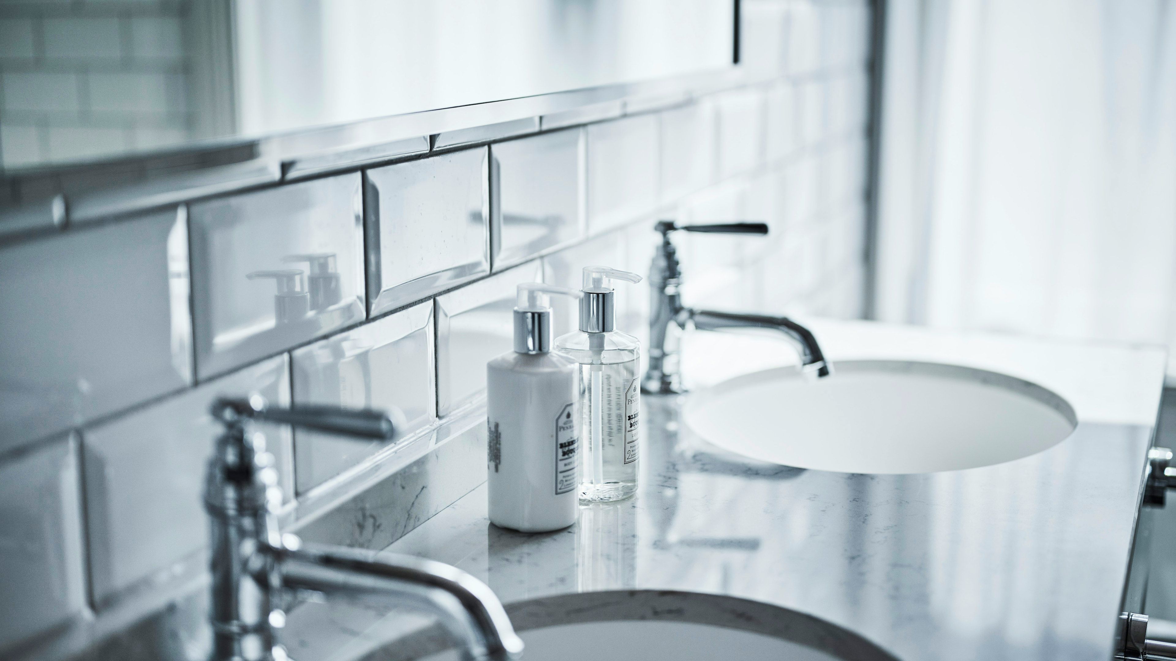 A modern bathroom with a large mirror, a sink, and two bottles of hand soap.
