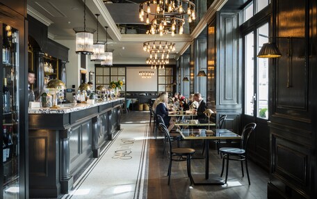 A spacious restaurant with a long counter, multiple dining tables, and a bar area with shelves of bottles.