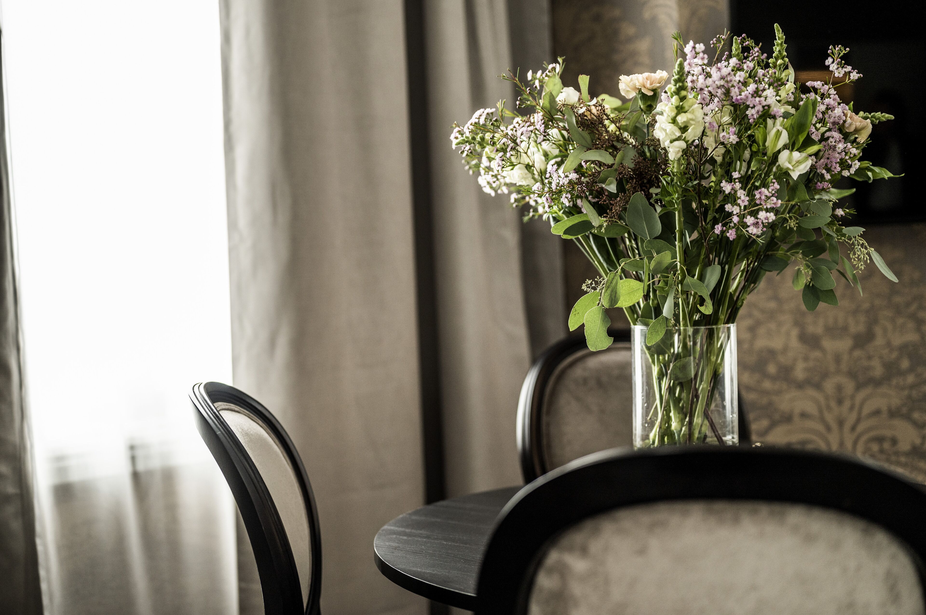Et bord med en vase blomster, to stole og en tapetvæg i baggrunden.