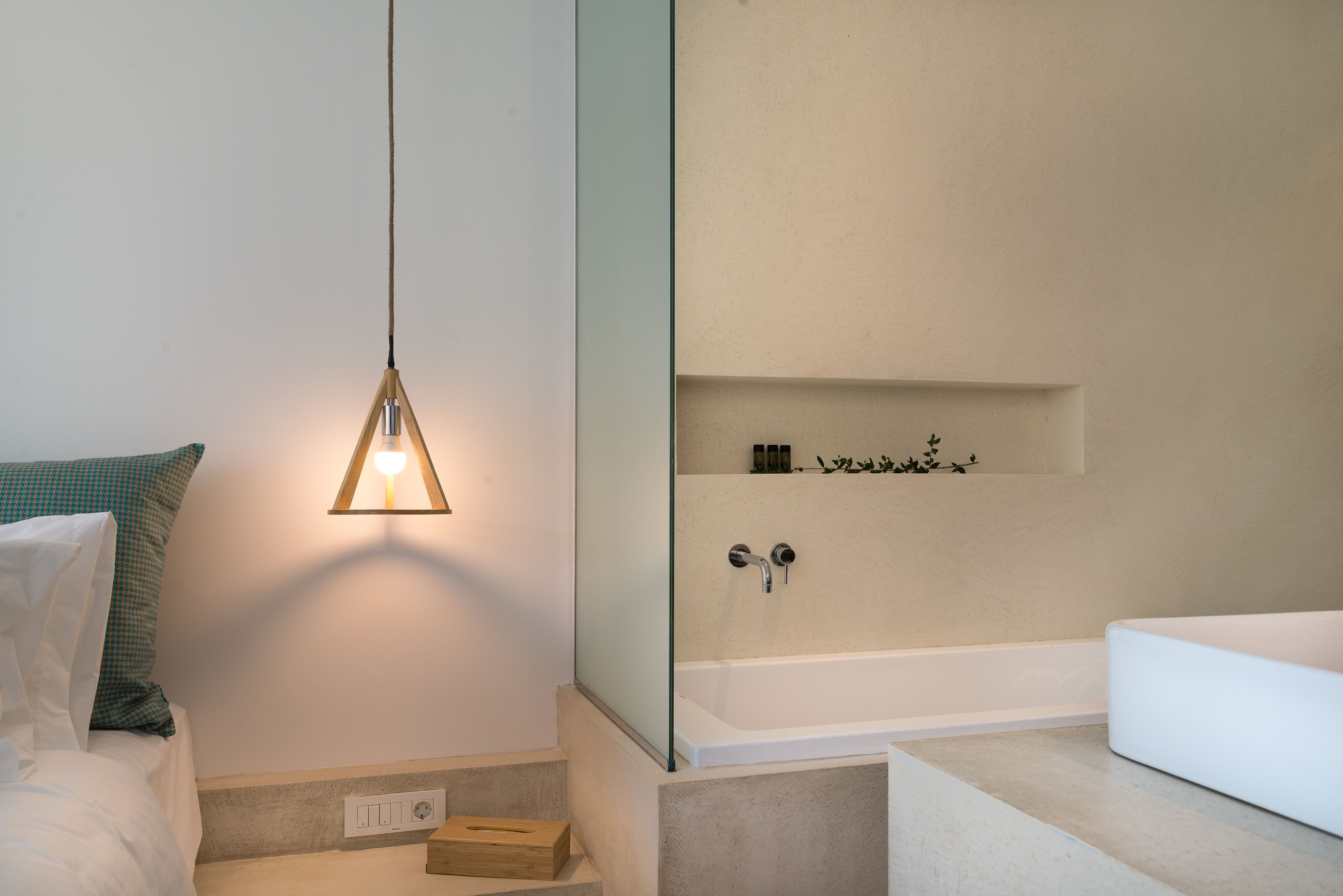 A modern bathroom with a bathtub, a glass shower enclosure, and a bedside table with a lamp.