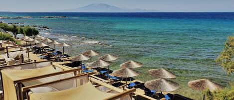 Un hôtel situé en bord de mer, doté de parasols en chaume et de cabanes en bois offrant une vue sur l’océan.