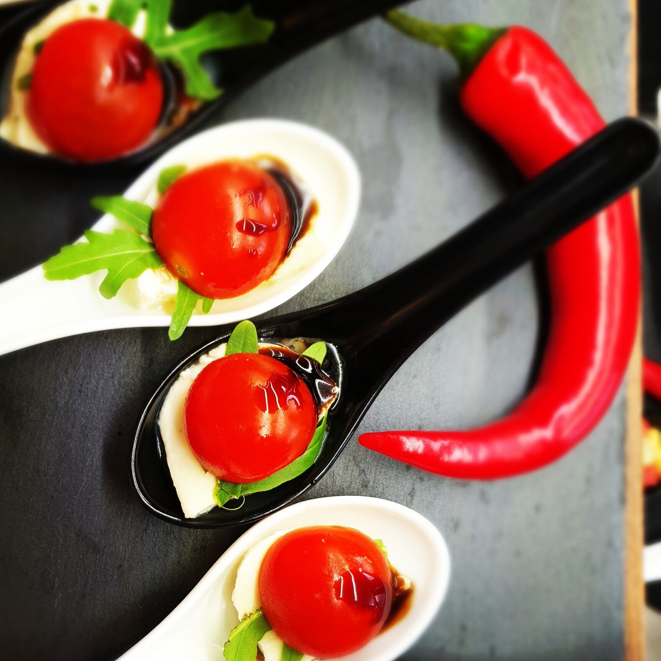 Tre skefulde mad med rød sauce, pyntet med grønne blade, på en mørk overflade med en rød chili.