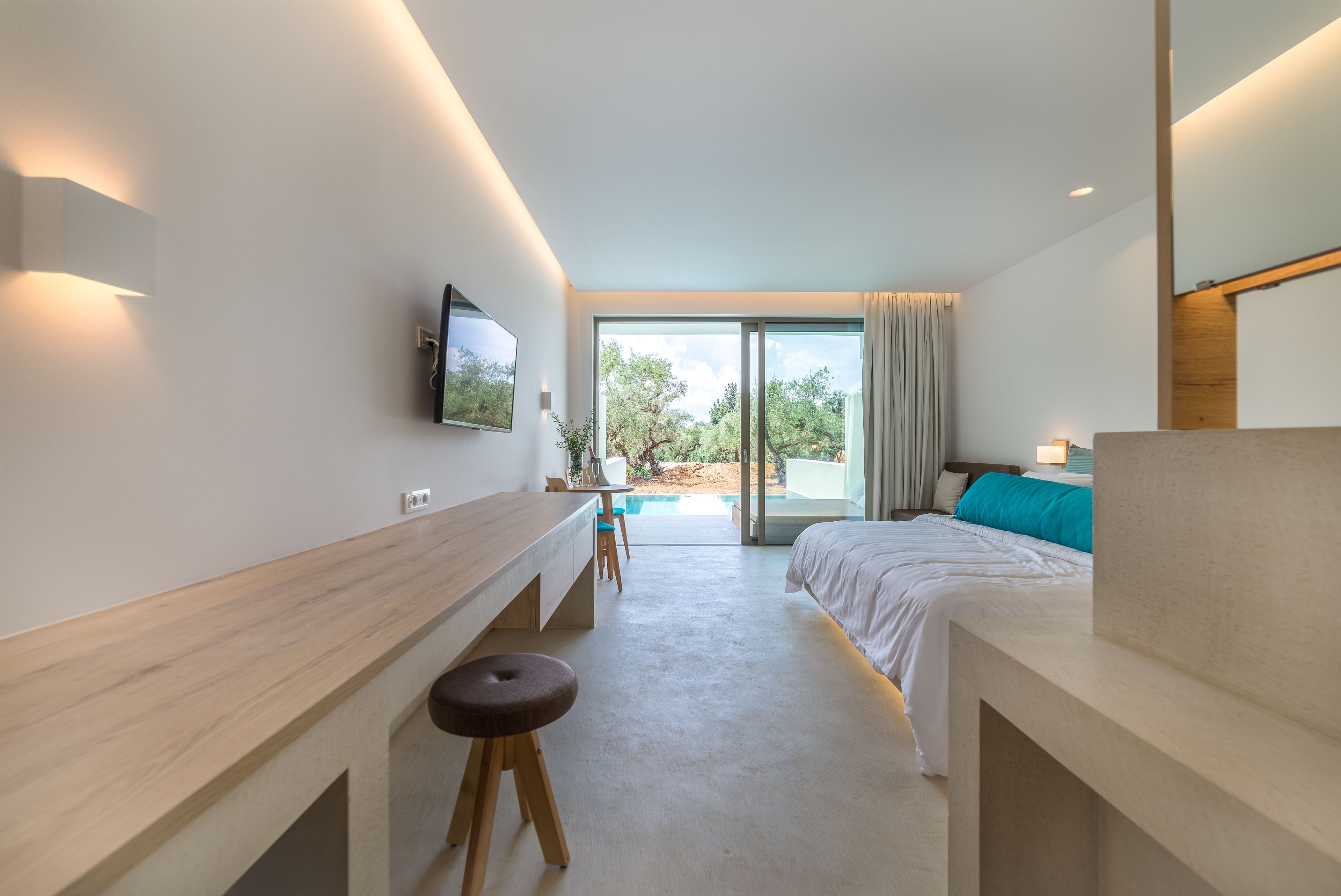 A modern hotel room with a bed, a desk, a TV, and a view of the outdoors.