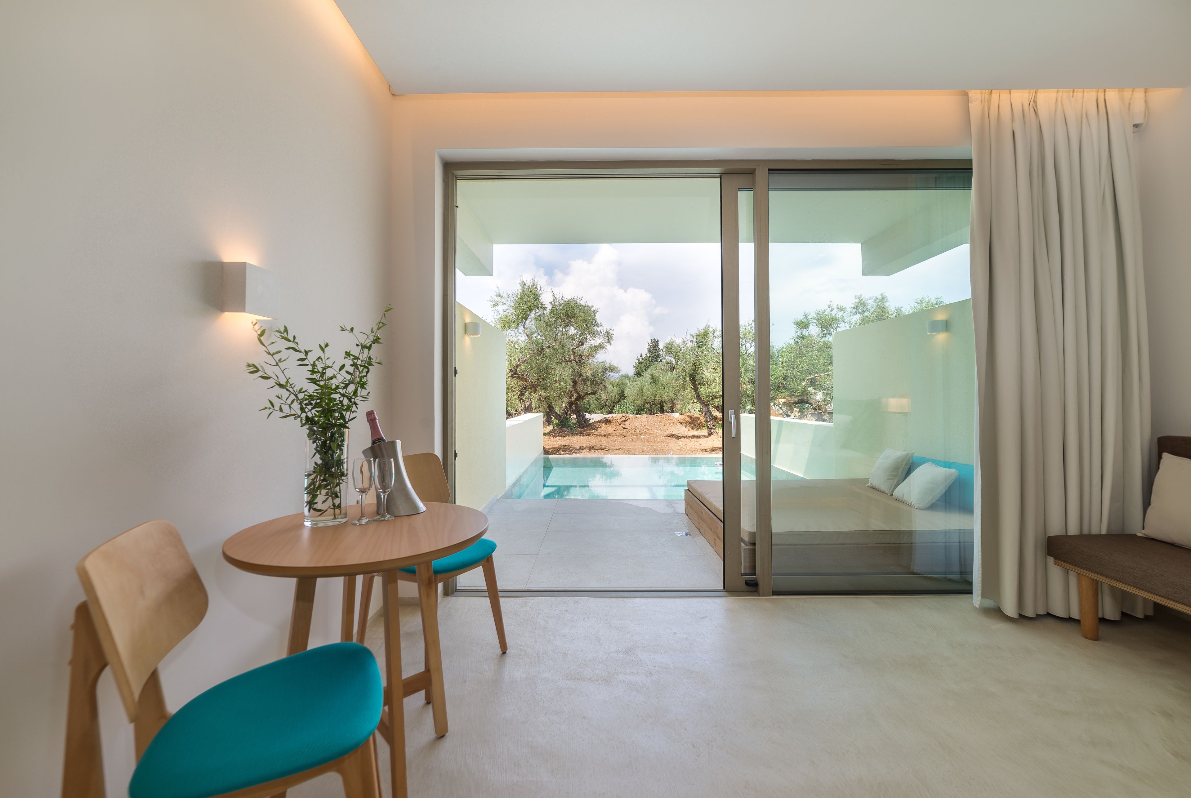 A modern room with a glass door leading to an outdoor pool area, a wooden table with chairs, and a sofa.