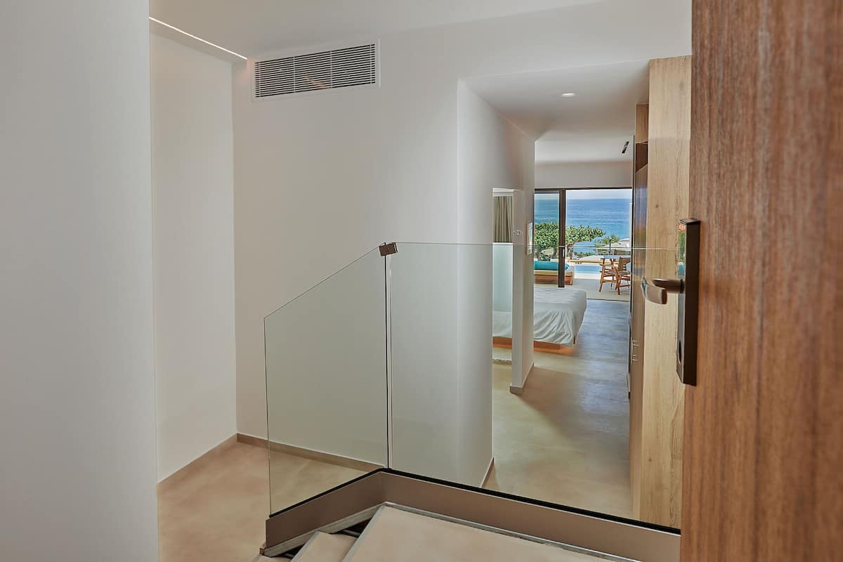 Un interior moderno con una escalera de cristal que lleva a un balcón con vistas al mar.