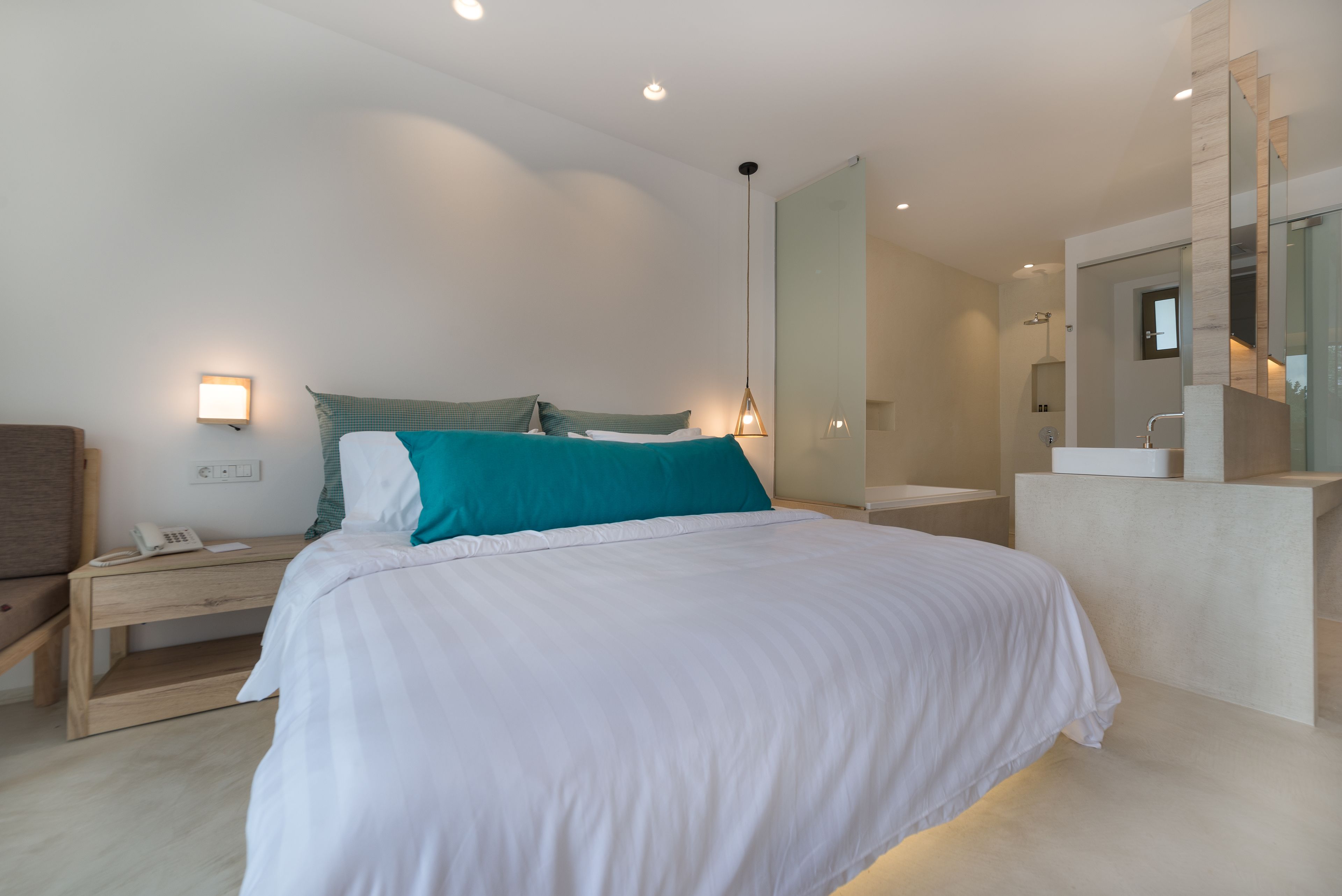 A modern bedroom with a large bed, bedside tables, a nightstand, a mirror, and a bathroom with a sink and shower.