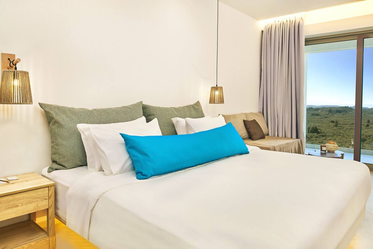 Un dormitorio moderno con una cama grande, una mesita de noche, una lámpara y vistas al exterior.