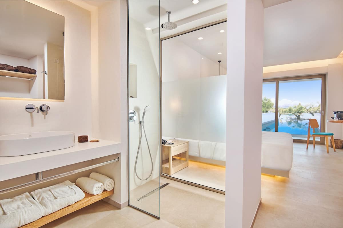 Un baño moderno con ducha envuelta en vidrio, tocador con lavamanos y repisa de madera con toallas.