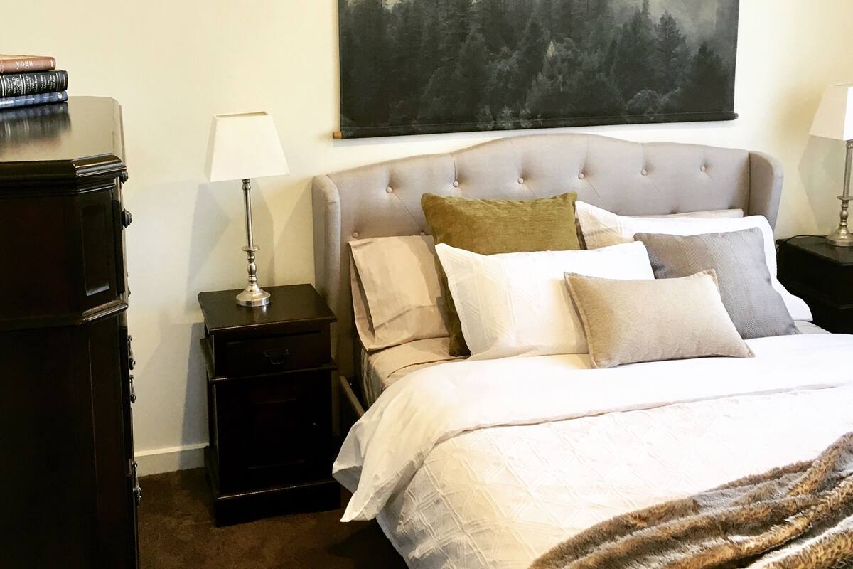 A bedroom with a large bed, a nightstand, a dresser, and a painting on the wall.