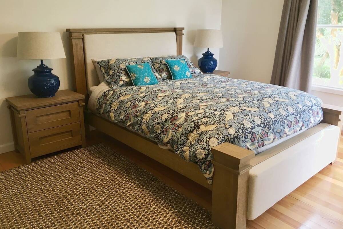 A bedroom with a wooden bed, two nightstands, a woven rug, and a window with curtains.