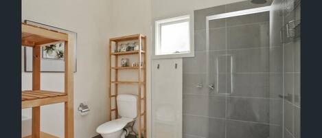 A bathroom with a toilet, wooden shelves, a shower with a glass door, and a window.