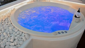 A hot tub with a blue light, surrounded by white pebbles, and a bottle of champagne. - Ariana Eco Suites - Adults Only (Santorini)