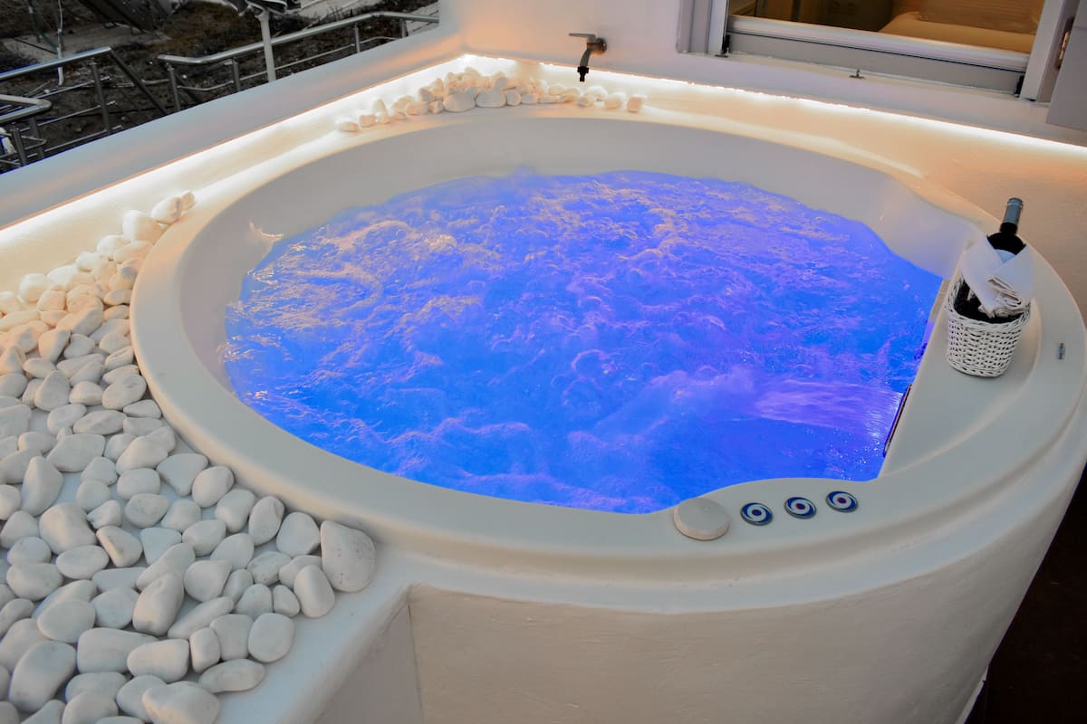 A hot tub with a blue light, surrounded by white pebbles, and a bottle of champagne.