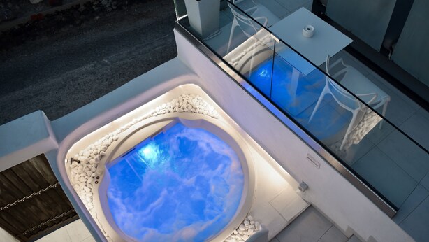 A modern indoor hot tub with a glass enclosure, surrounded by white pebbles and a white wall. - Ariana Eco Suites - Adults Only (Santorini)