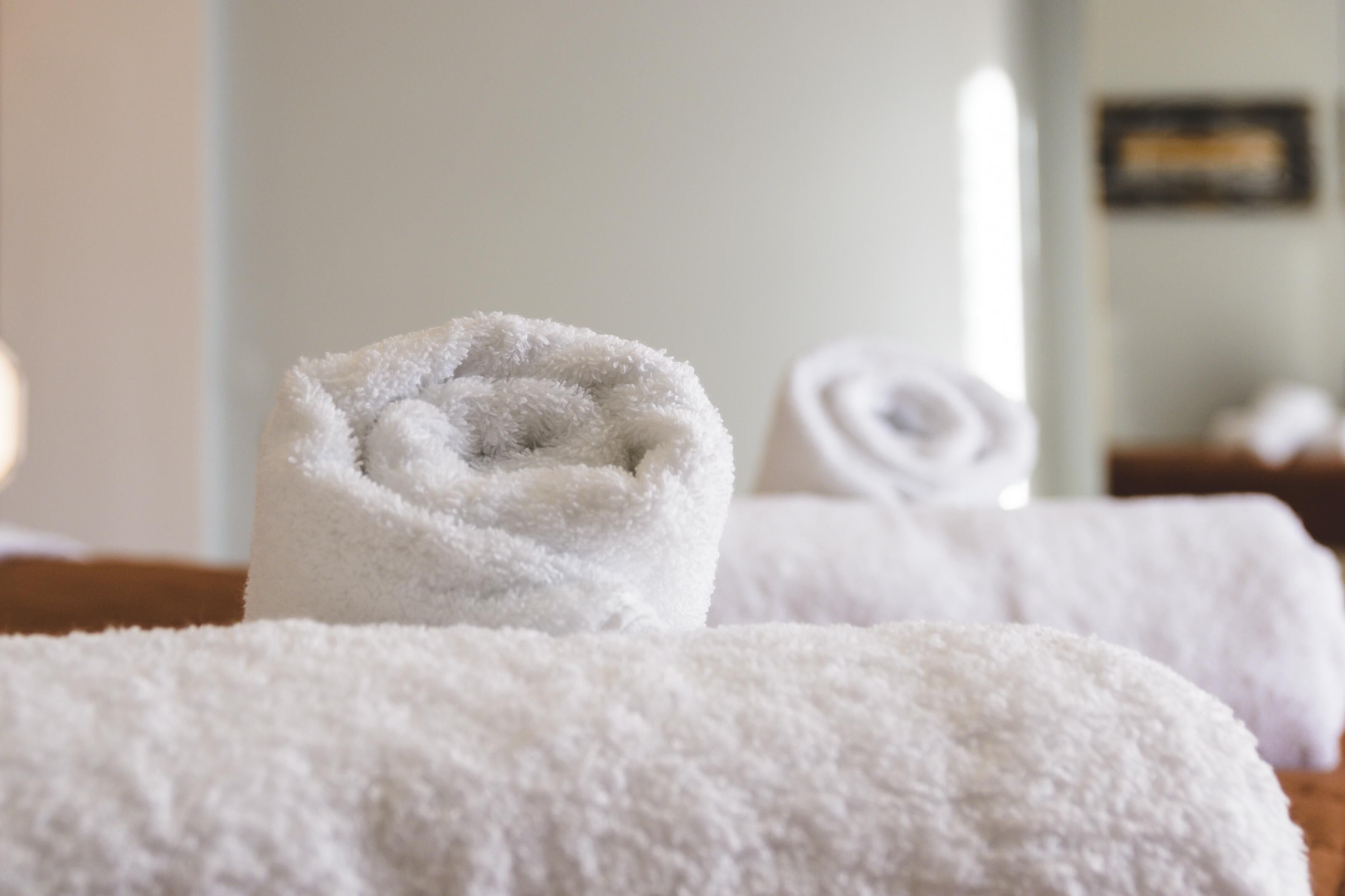 A neatly folded white towel on a wooden surface, likely in a hotel room.