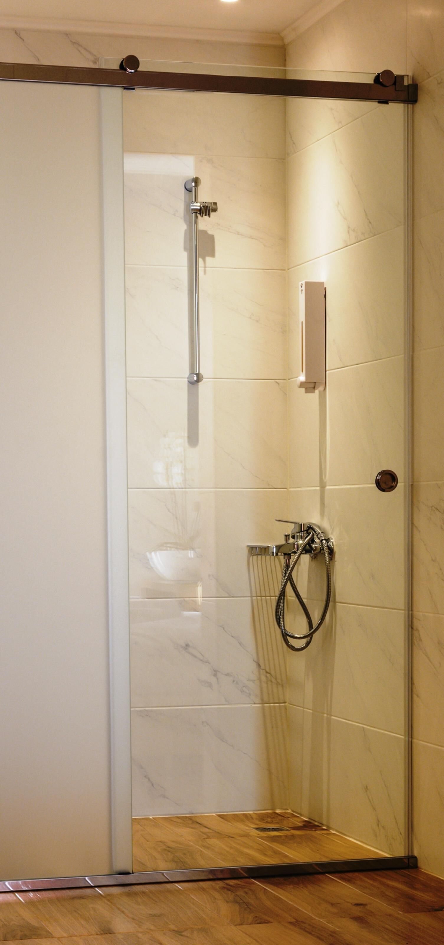 A glass-enclosed shower with a handheld showerhead and a wall-mounted control panel.
