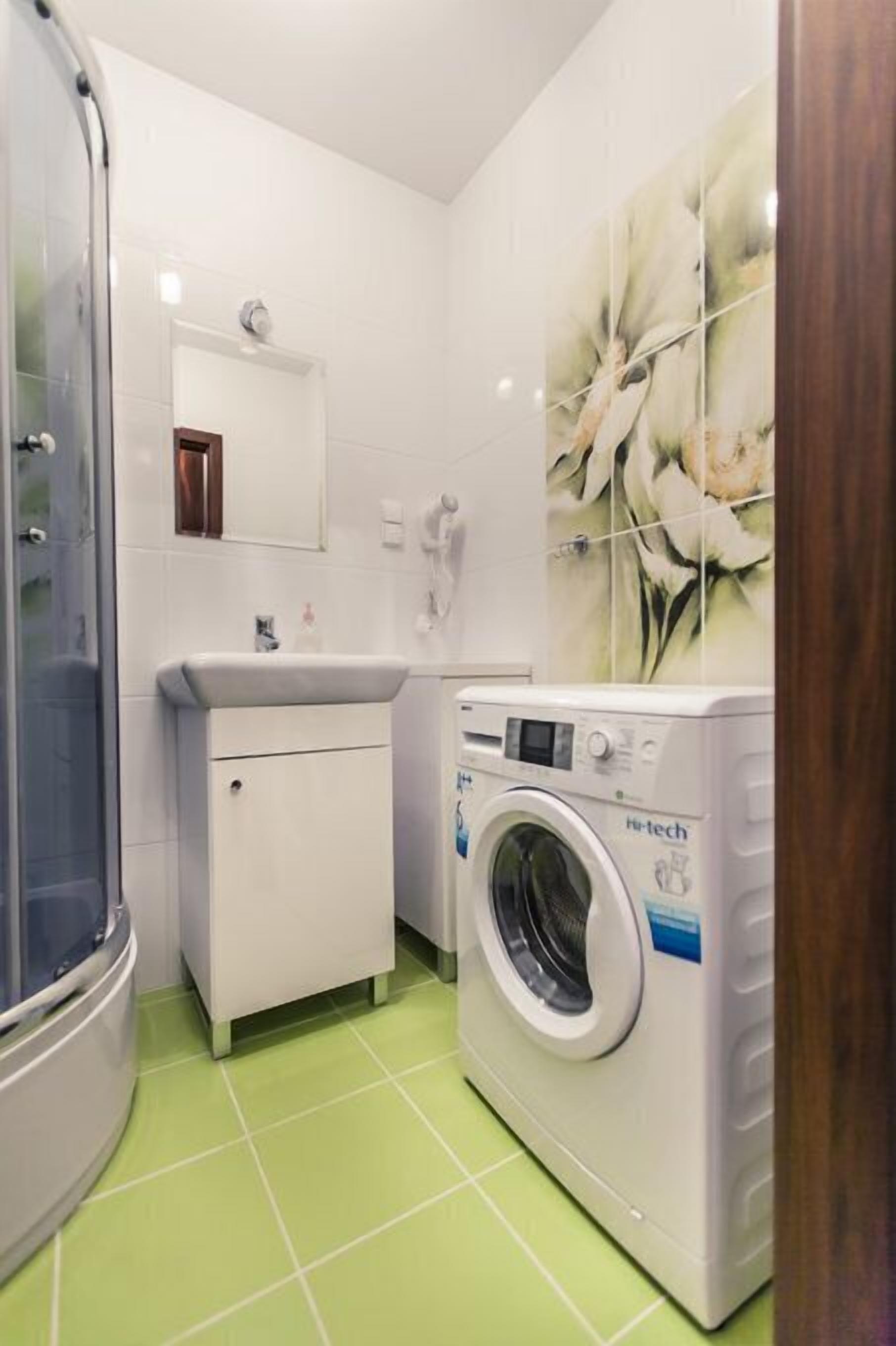 A compact bathroom with a shower, a sink, a washing machine, and a mirror.