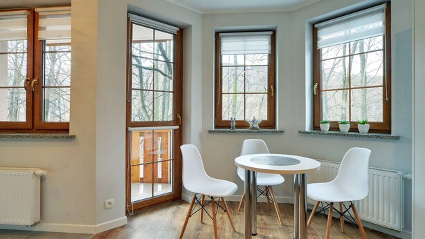 A room with a round table and four white chairs, large windows with wooden frames, and a radiator on the wall. - EverySky Lesny Dom (Karpacz)