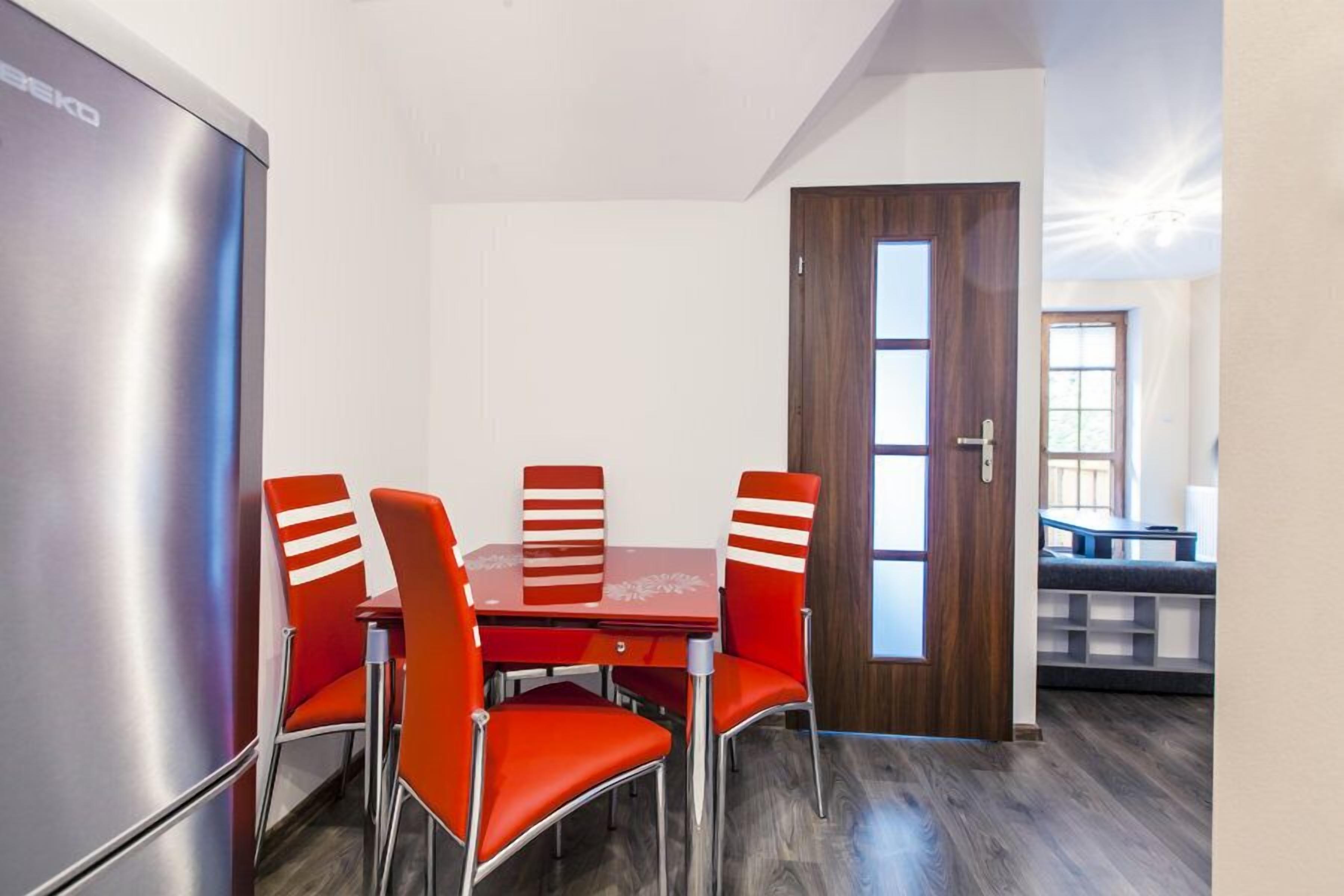 A dining area with a table and four chairs, a refrigerator, and a wooden door.