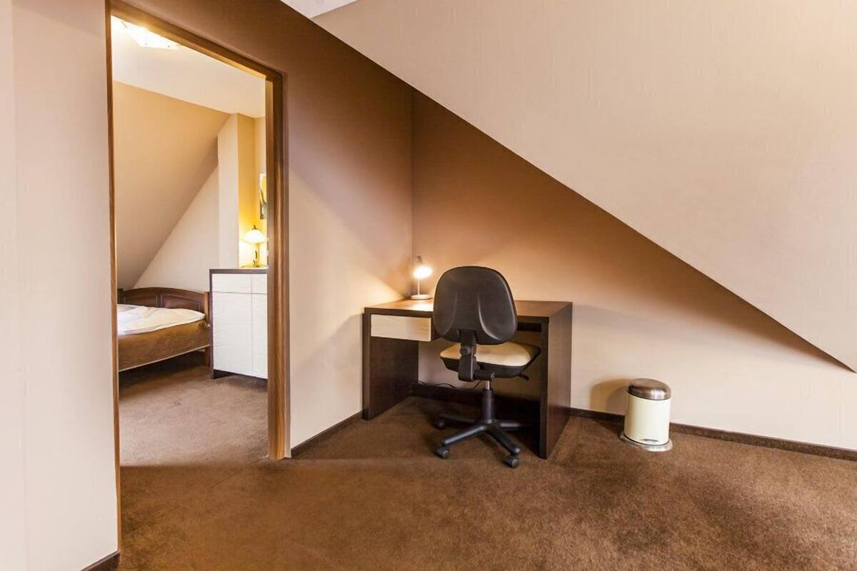 Un dormitorio con techo inclinado, un escritorio con silla, una mesita de noche y una lámpara.