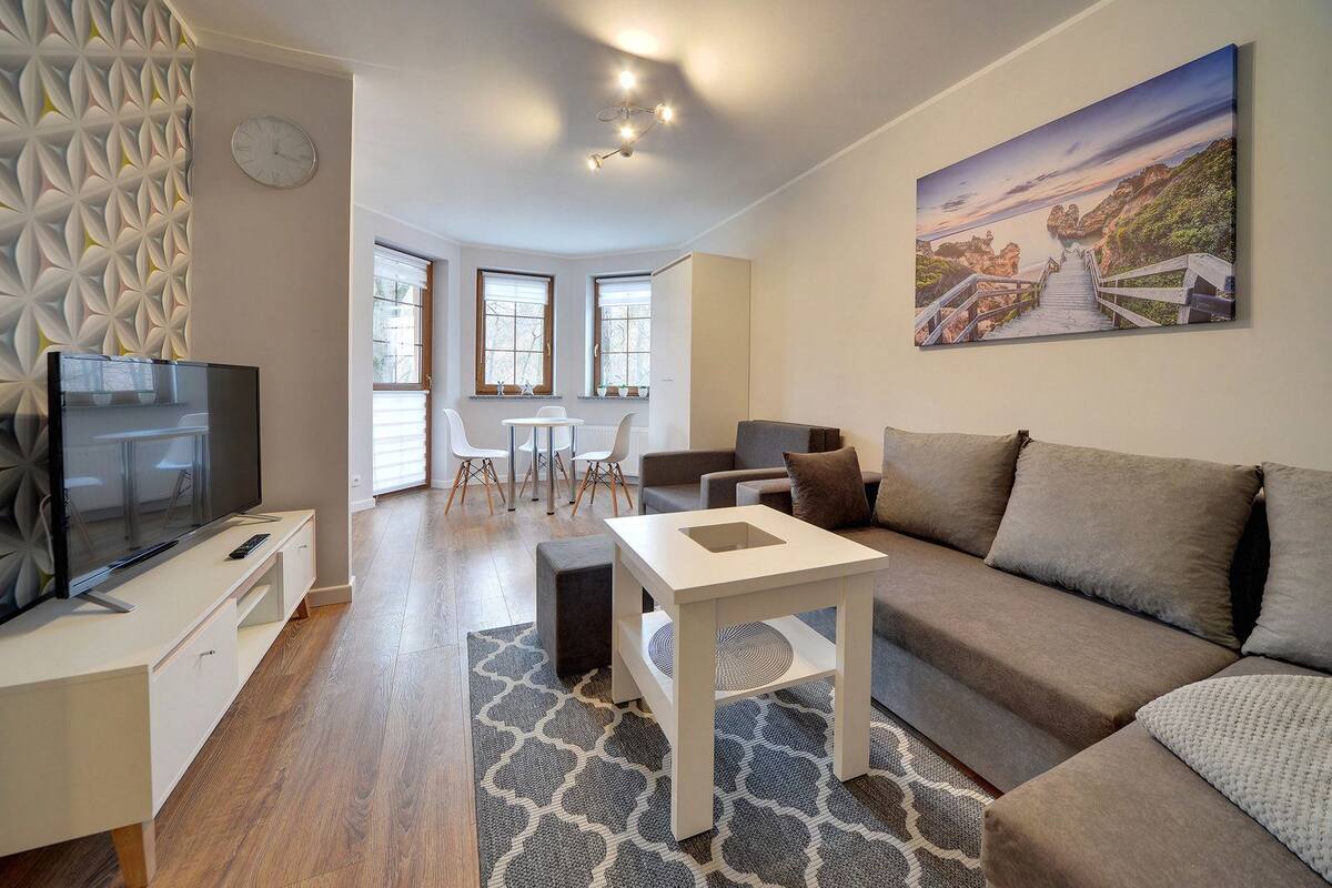 Una sala de estar moderna con un televisor de pantalla plana, un sofá, una mesa de centro y un comedor con una mesa y sillas.
