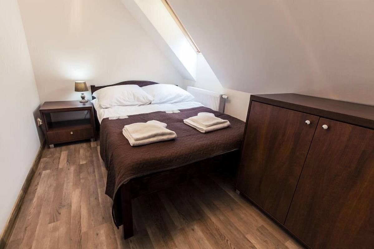 Un dormitorio pequeño y ordenado con cama, mesita de noche, armario y ventana que deja entrar luz natural.