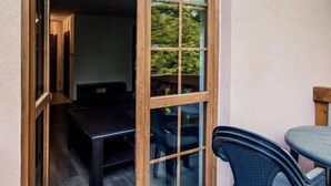 A room with a sliding glass door leading to a balcony, a small table with chairs, and a bed with a headboard. - EverySky Lesny Dom (Karpacz)