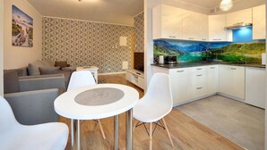 A modern living room with a sofa, a dining table with chairs, a kitchen with white cabinets and a large window, and a patterned wall. - EverySky Lesny Dom (Karpacz)