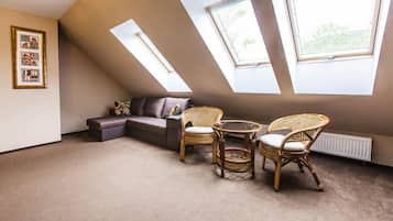 A room with a sloped ceiling, two large windows, a sofa, two wicker chairs, and a small table.